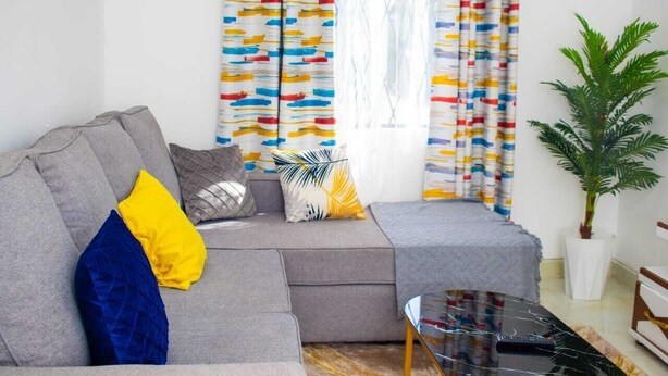 Una sala de estar moderna con un sofá gris, cortinas coloridas, una mesita y una planta en maceta.