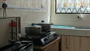Una cocina con paredes de azulejos blancos, una mesa de madera, un refrigerador y una ventana con cortinas estampadas.