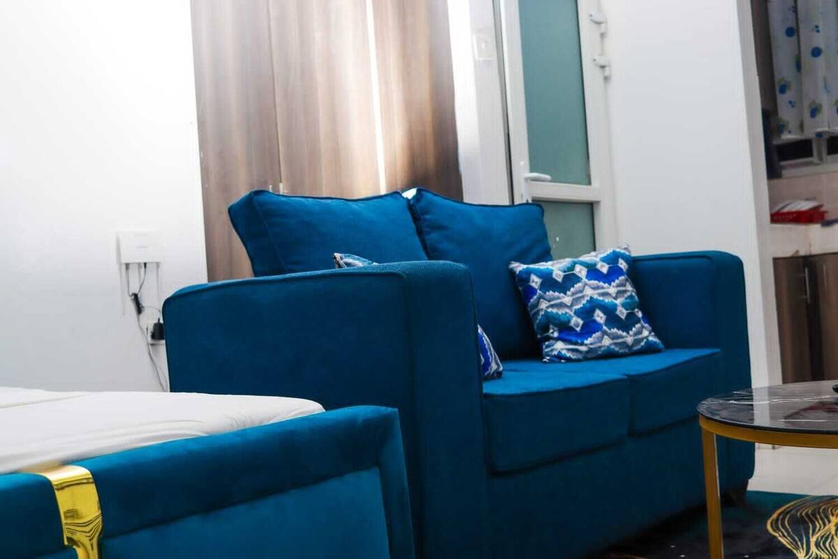 Ein blaues Sofa mit gemusterten Kissen in einem Zimmer mit weißer Wand und einem fenster mit Vorhängen.