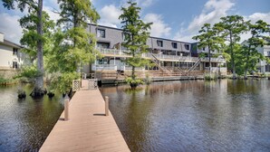 Une propriété située au bord de l’eau, dotée d’un quai en bois menant à un bâtiment comportant plusieurs balcons et un espace extérieur couvert.