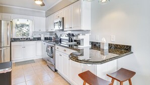 Une cuisine moderne avec des armoires blanches, un comptoir en granit, un four à micro-ondes encastré et un ventilateur de plafond.