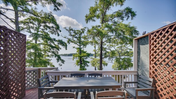 Une terrasse en bois avec une table et des chaises, donnant sur un lac bordé d’arbres.