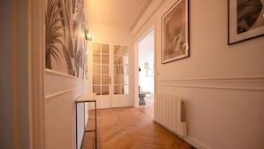 Un couloir doté d’un plancher en bois, d’un mur recouvert de miroirs et d’une porte blanche donnant sur une pièce.