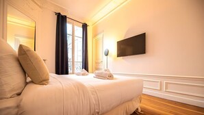 Une chambre avec un grand lit, un téléviseur à écran plat fixé au mur et une fenêtre avec des rideaux.