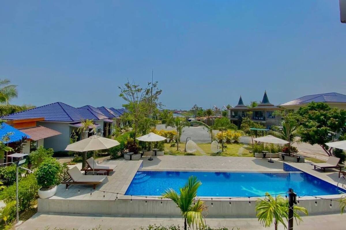 A resort with a central swimming pool, lounge chairs, umbrellas, and tropical landscaping.