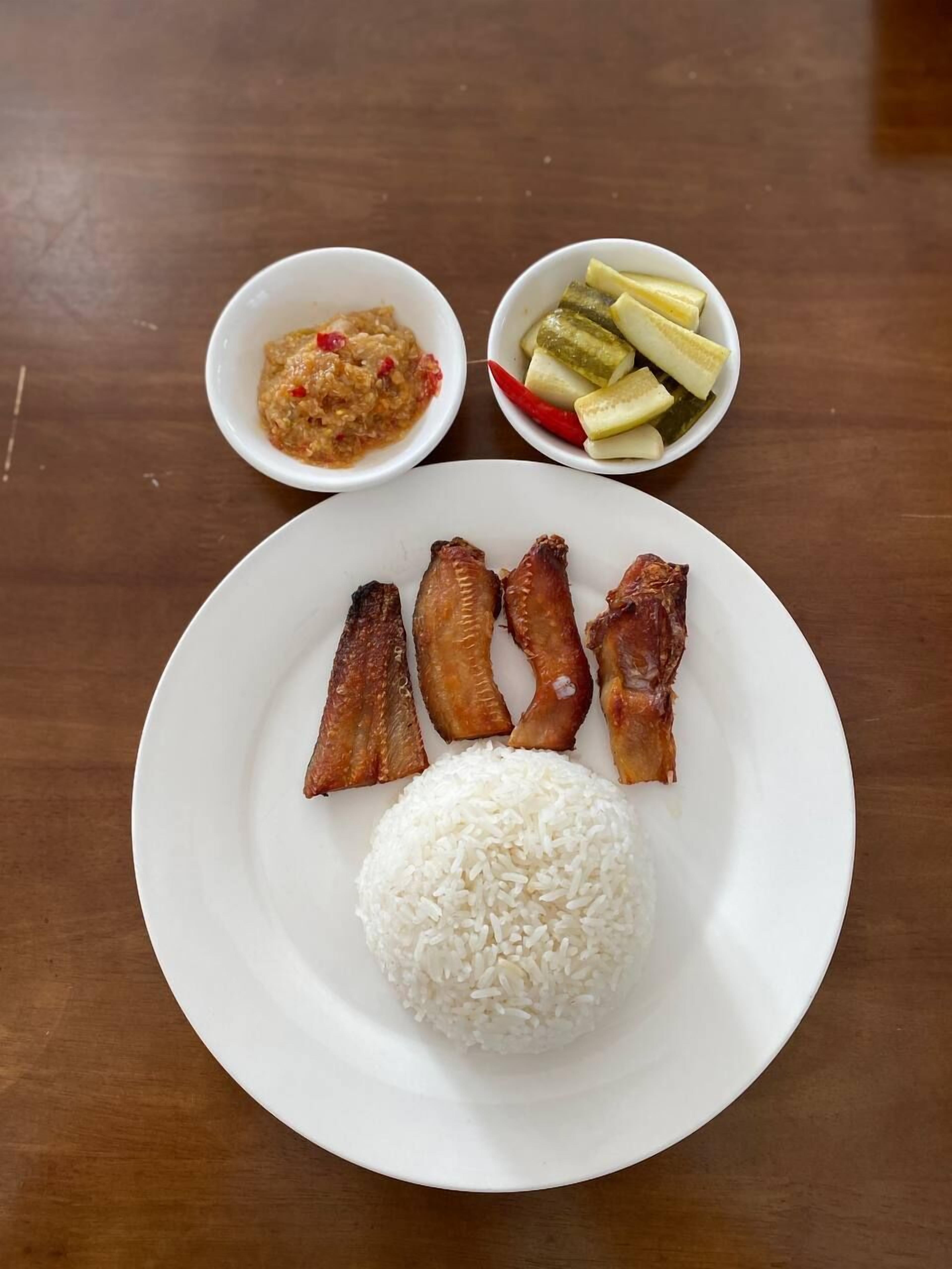 Un plato con arroz blanco, varios trozos de pollo frito, un tazón de sambal y un tazón de verduras encurtidas.
