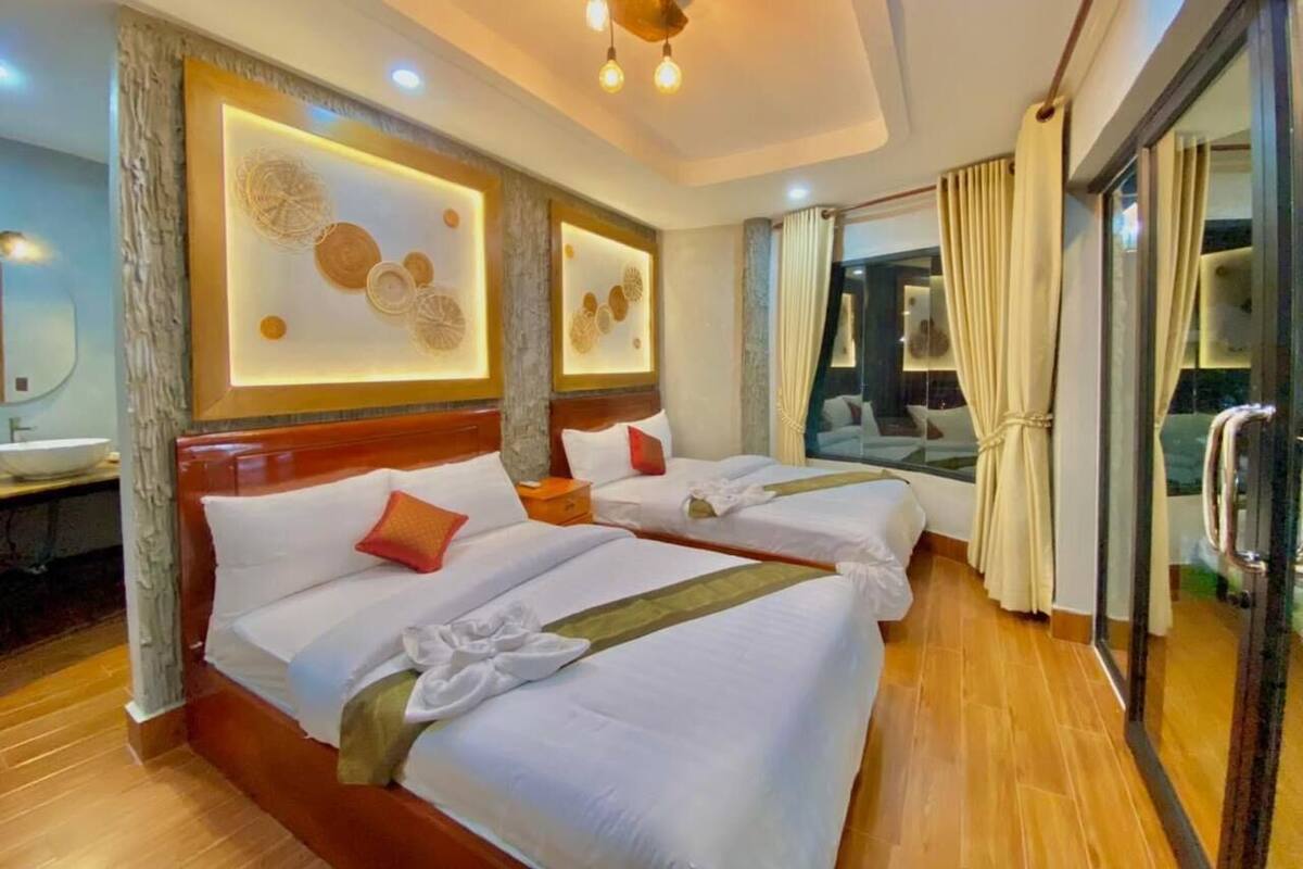 A hotel room with two beds, a wooden floor, a large window with curtains, and a modern ceiling light fixture.