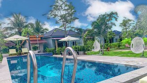 A swimming pool with metal railings, surrounded by lounge chairs and umbrellas, with houses and greenery in the background. - Finance Boutique (Kampot)