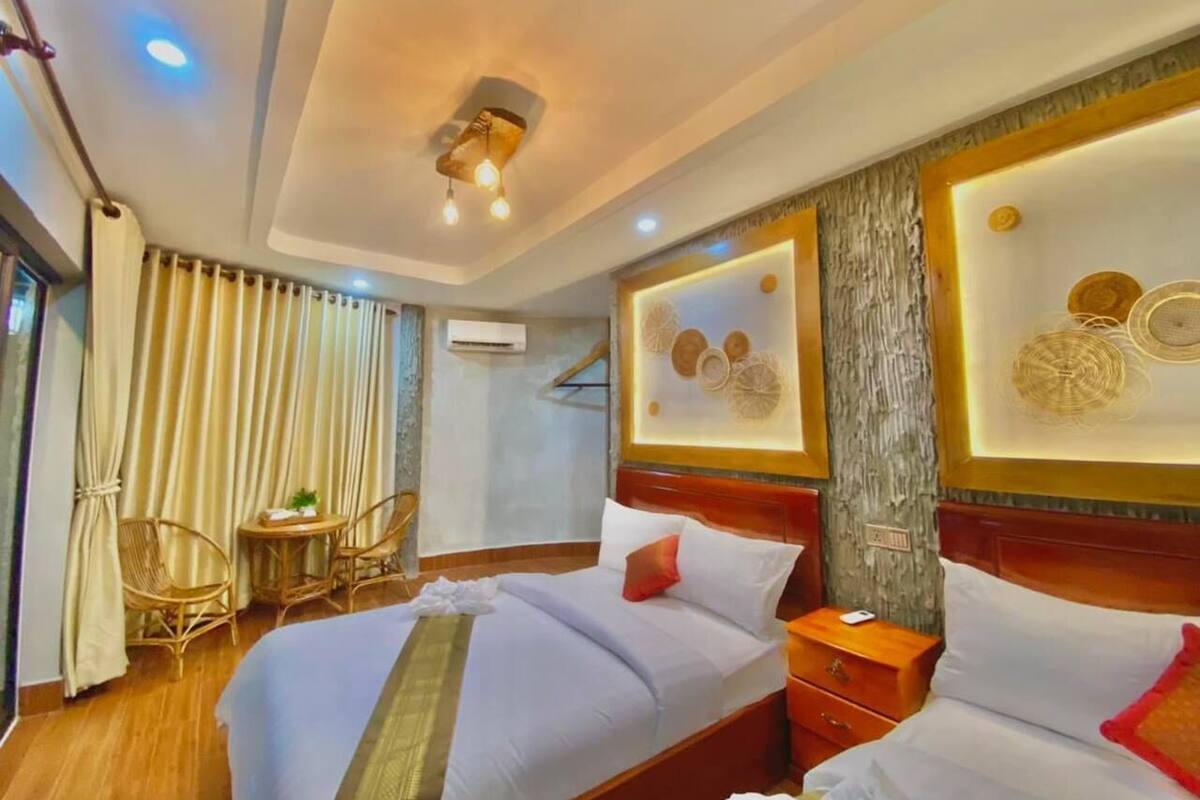 A hotel room with a large bed, two bedside tables, a small table with chairs, and a large window with curtains.