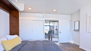 A bedroom with a bed, a wardrobe, and a sliding glass door leading to a balcony. - Historic Modern Apartment! Park Free w/ DT Views! (Spokane)