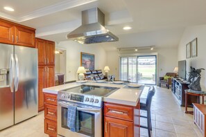 A spacious kitchen with a central island, stainless steel appliances, wooden cabinets, and a large window providing a view of the outdoors. - Spacious Condo w/ Mtn Views in Palm Desert! (Palm Desert)