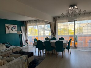 Una sala moderna con sofá, una mesa de comedor con sillas, una obra de arte con un mapa mundial y un ventanal con vistas a edificios y árboles.