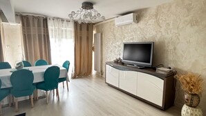 Una zona pranzo con tavolo e sedie, una televisione su un mobile e un vaso con piante essiccate.