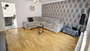 Ein Wohnzimmer mit einem grauen Ecksofa, einem kleinen runden Couchtisch und einer Wand mit Muster.