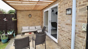 Eine überdachte Terrasse mit Korbmöbeln, einer Schiebetür und einer Ziegelwand.