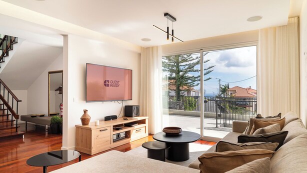 A modern living room with a flat-screen TV, wooden entertainment unit, and a sofa. - GuestReady - Lush Stay in Funchal (Funchal)
