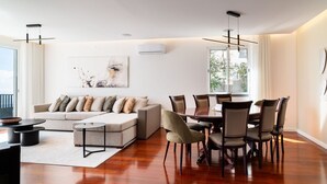 A modern living room with a sofa, coffee table, dining table with chairs, and a large window. - GuestReady - Lush Stay in Funchal (Funchal)