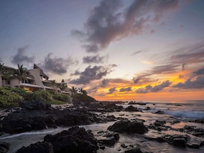 A coastal resort with modern architecture, rocky shoreline, and a sunset view.