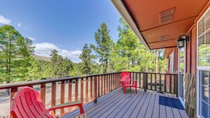 A wooden deck with two red Adirondack chairs, a wooden railing, and a view of a forested area. - 1 Mi to Alto Lake: Mtn-View Home w/ Large Yard! (Alto)