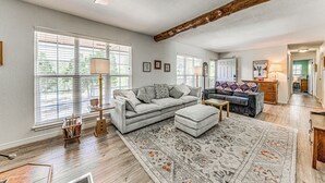A spacious living room with a large sofa, ottoman, and a patterned rug. There is a wooden ceiling beam, a ceiling fan, and a window with blinds. - 1 Mi to Alto Lake: Mtn-View Home w/ Large Yard! (Alto)