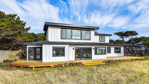 Een modern huis met twee verdiepingen, een terras, grote ramen en een houten hek op de achtergrond.