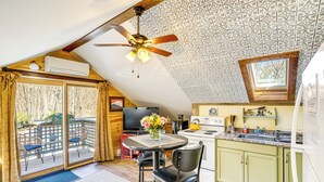 Une cuisine équipée d’un ventilateur de plafond, d’une table à manger avec des chaises, d’un téléviseur et d’une fenêtre donnant sur les arbres.