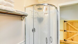 Une douche avec des portes en verre, une porte en bois et un porte-serviettes avec des serviettes pliées.