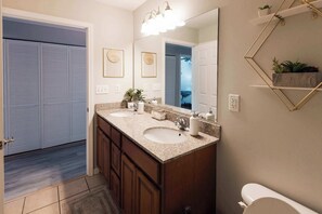 Un bagno con due lavandini, uno specchio grande e un water. Ci sono piante su mensole e una porta che offre vista sull'esterno.