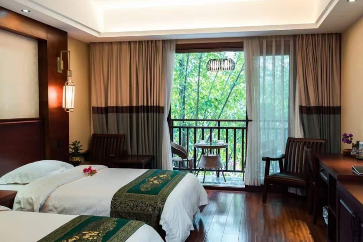 A hotel room with two beds, a balcony with a table and chairs, and a desk with a chair.