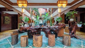 A spacious lobby with a central wooden table, multiple wooden stools, and a variety of potted plants. - XiShuangBanNa BaoYu Vaction Hotel (Xishuangbanna Dai)