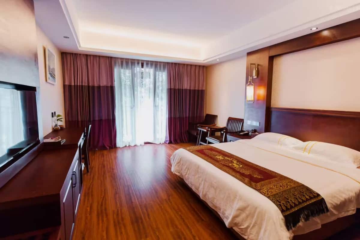 A hotel room with a large bed, a desk with a chair, a TV, and a window with curtains.