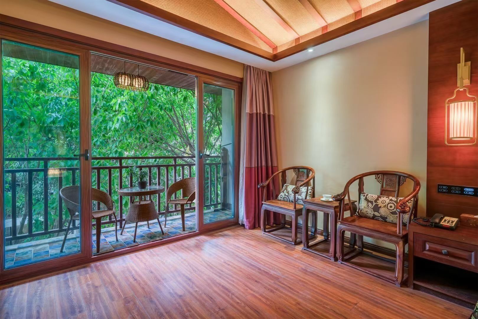 Une pièce dotée d’un plancher en bois, de grandes portes-fenêtres coulissantes donnant sur un balcon, de deux chaises en bois, d’une petite table et d’un téléphone fixé au mur.