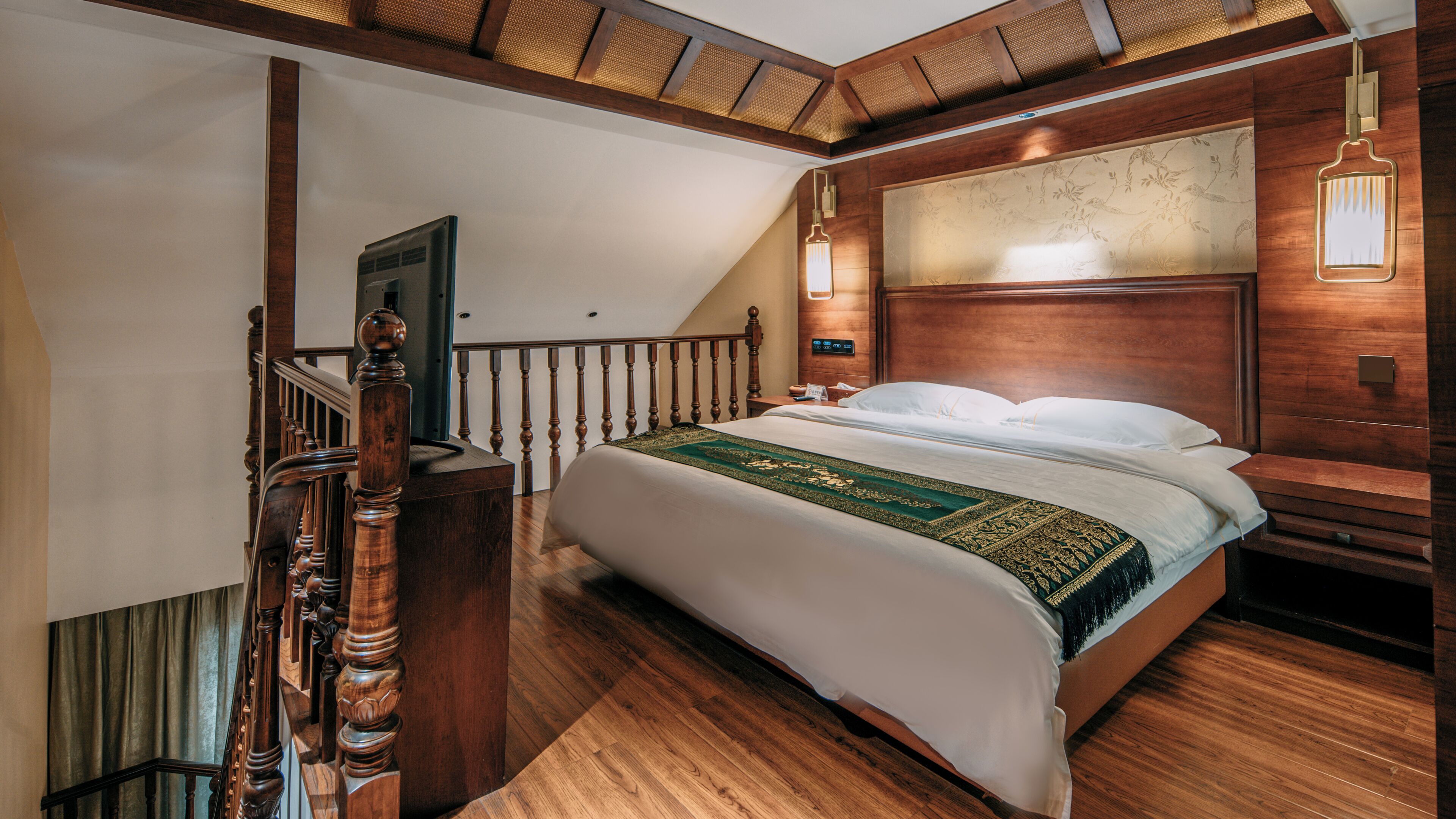 A bedroom with a wooden bed, a nightstand, a wall-mounted lamp, and a staircase with wooden railings.