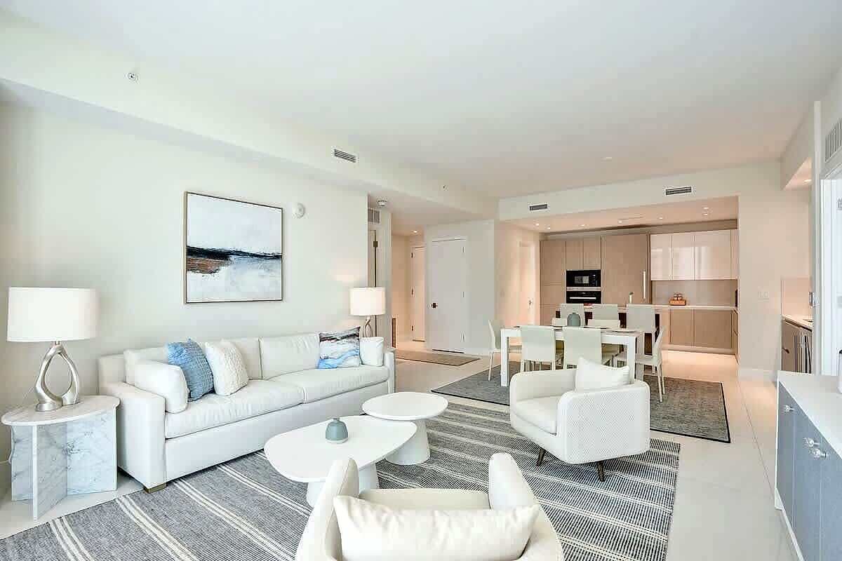 A modern living room with a sofa, two white armchairs, a coffee table, and a dining area with a table and chairs.