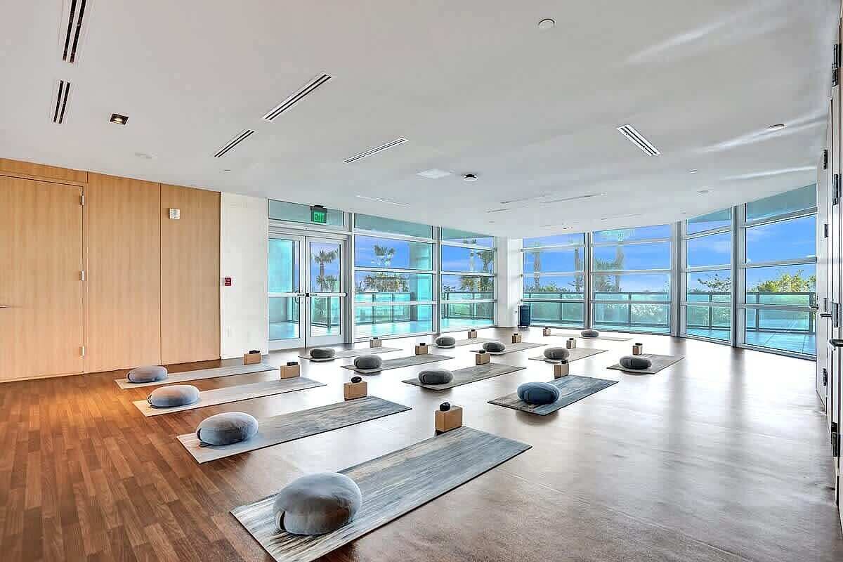 Una habitación amplia con ventanas grandes, suelo de madera y colchonetas de yoga dispuestas para practicar.