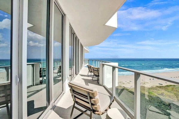 A balcony with a view of the ocean, large windows, and a seating area.