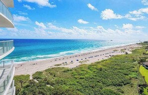 A beach with a clear view of the ocean, a sandy shore, and a building with a balcony overlooking the beach.