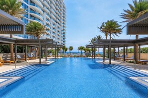 A hotel pool with sun loungers and palm trees.