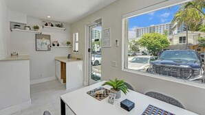 A modern kitchen with white cabinetry, a countertop, and a window overlooking a street with parked cars and buildings. - Steps to Beach Studio Suite | Pool & Las Olas (Fort Lauderdale)
