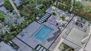 An aerial view of a rooftop pool area with a rectangular pool, lounge chairs, and surrounding greenery. - Eden 1BR | Steps to Fort Lauderdale Beach (Fort Lauderdale)
