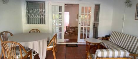A covered patio with a tiled floor, a table with chairs, a sofa, and a ceiling fan.