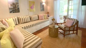 A living room with a striped sofa, a wooden chair, and a small table with a vase. - Charming Condo Sunset Palms #61 Holetown Beach pool access WiFi (Holetown)