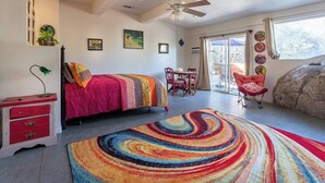 Un dormitorio con cama, escritorio y silla. Cuenta con un ventanal grande y un ventilador de techo.