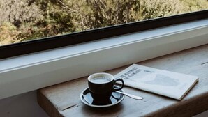 Uma chávena de café sobre uma mesa de madeira, com vista para uma paisagem natural.