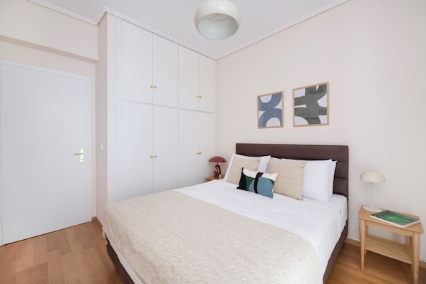 A bedroom with a large bed, white wardrobe, and two wall art pieces.