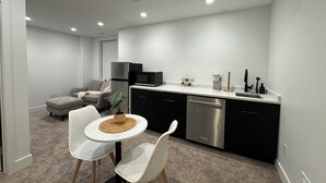 Eine moderne Küche mit Essbereich, ausgestattet mit einem weißen Tisch, zwei weißen Stühlen, einem grauen Sofa und einem schwarzen Kühlschrank.
