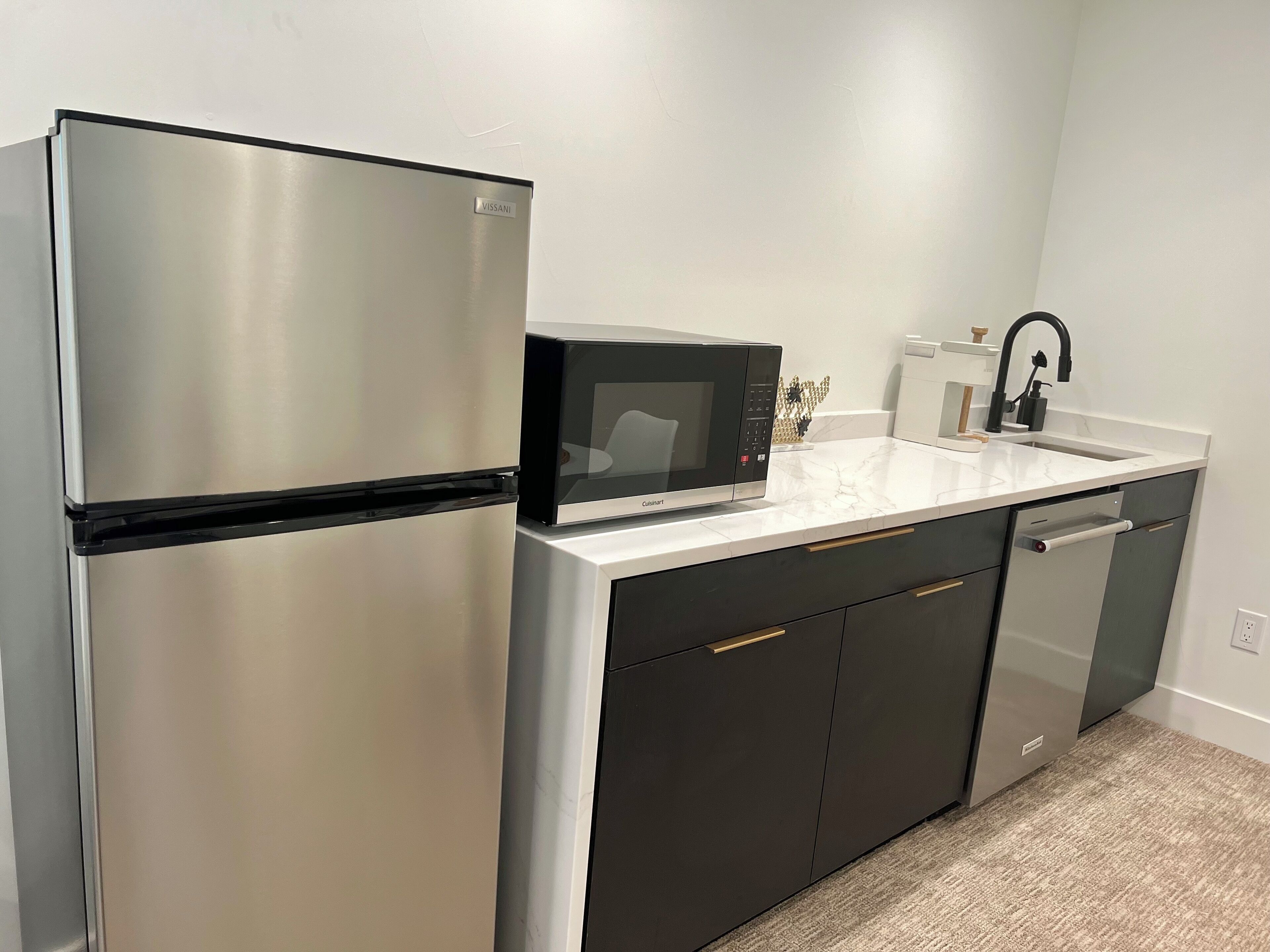 A compact kitchen with a stainless steel refrigerator, a black microwave, and a modern sink.