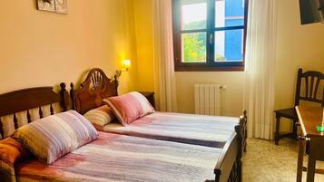 Una habitación con dos camas de madera, una silla, una mesa, una lámpara y un ventanal con cortinas.