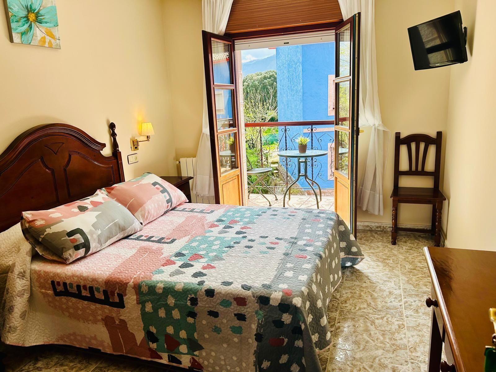 A bedroom with a bed, a chair, a small table, and a balcony with a view.