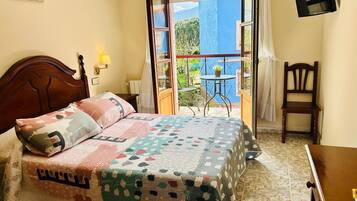 A bedroom with a bed, a chair, a small table, and a balcony with a view.